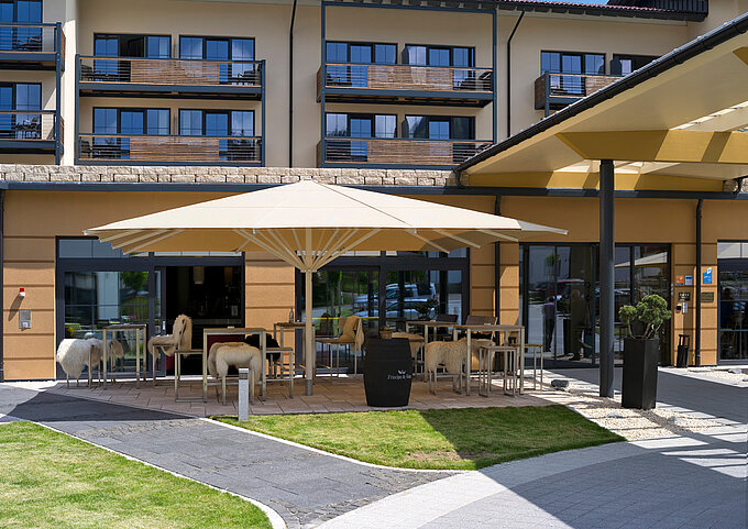 Beiger Sonnenschirm vor einem Hotel als Schattenspender