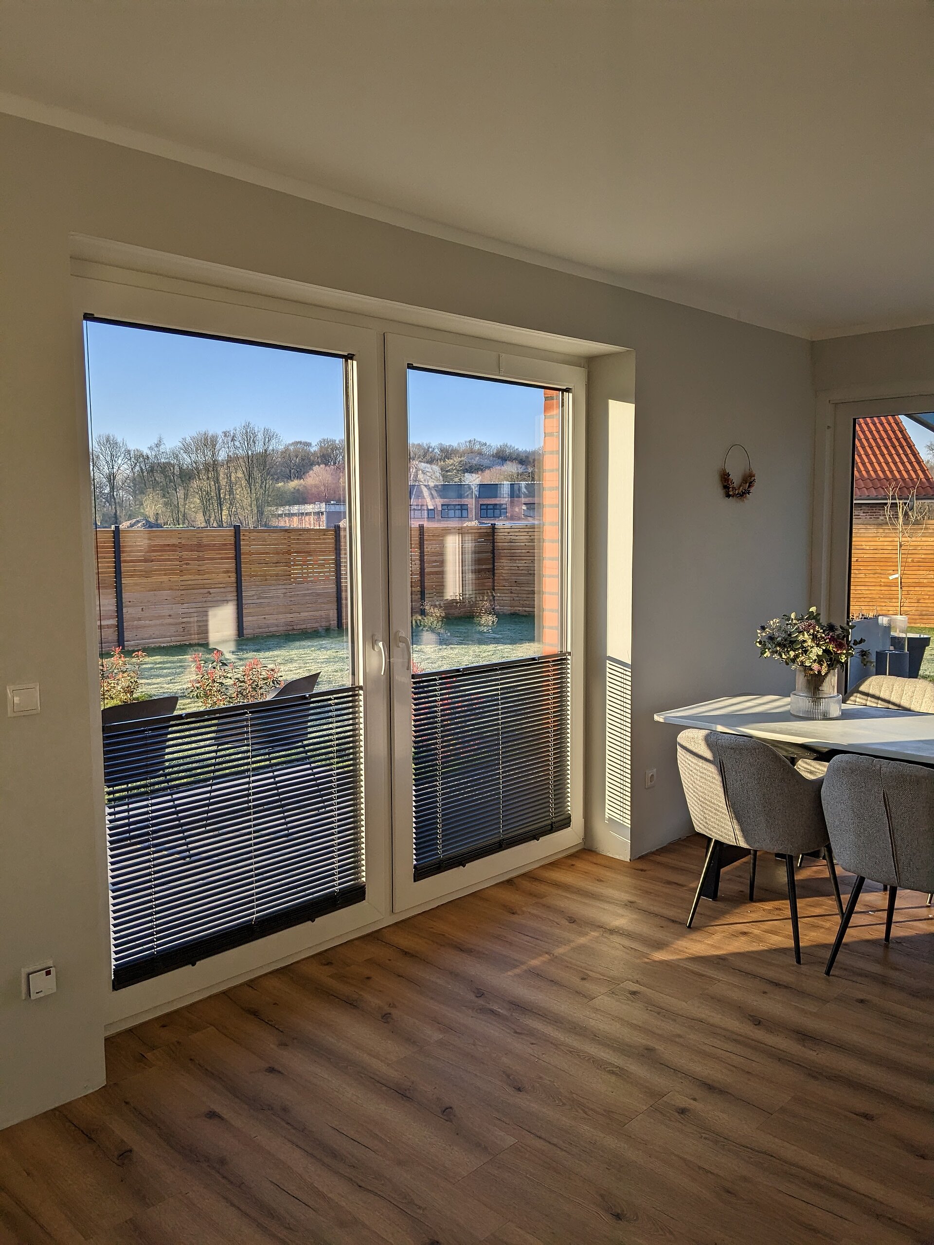 Esszimmer mit bodentiefen Fenstern und Twinline-Jalousien im unteren Bereich für Sichtschutz und Lichtregulierung.