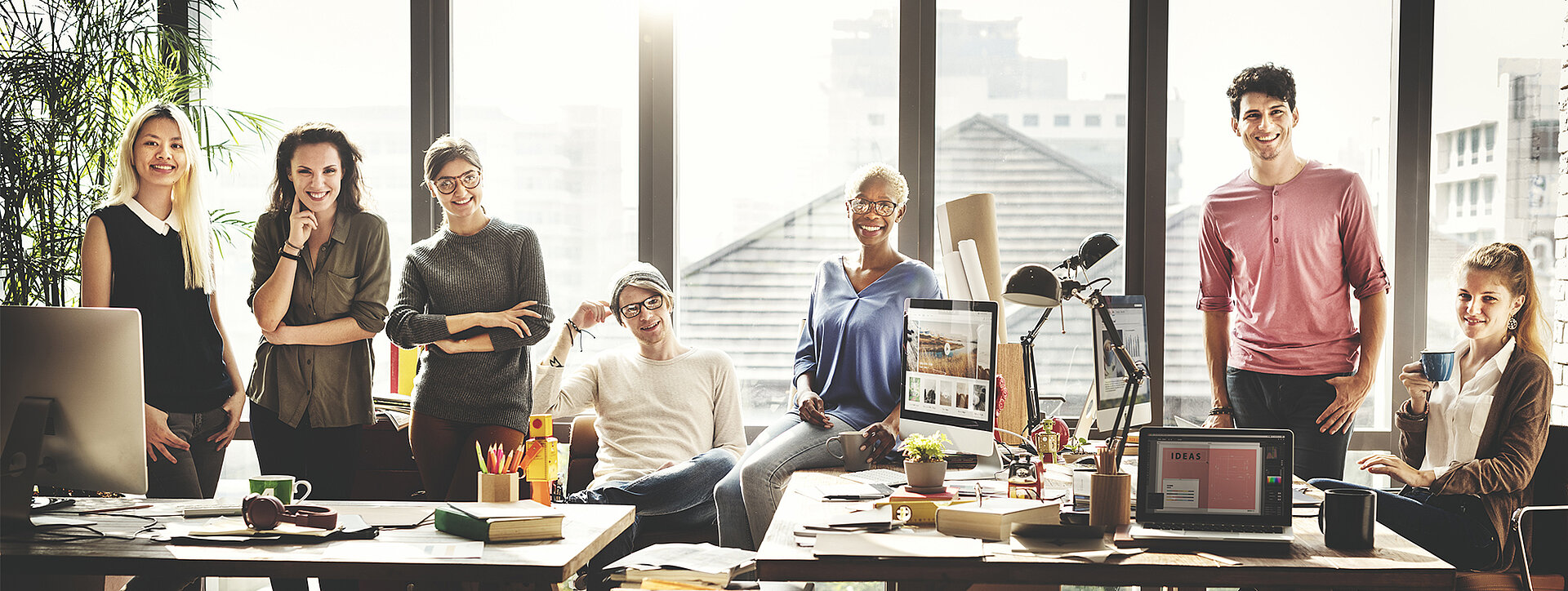 Gruppe von Mitarbeitern in einem modernen Büro mit grossen Fenstern und viel Tageslicht, umgeben von Arbeitsplätzen.