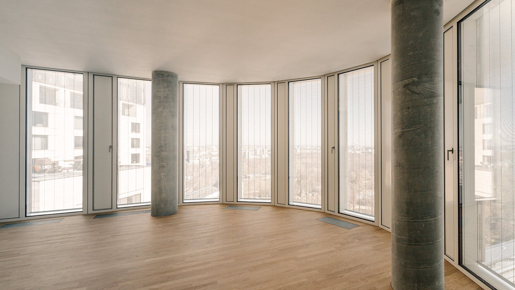 Innenraum mit bodentiefen Fenstern und vertikalen MHZ-Metallbehängen Senn vor einer Panorama-Aussicht.