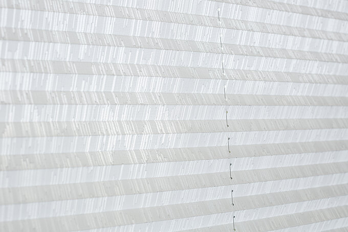 Detailaufnahme eines weissen Plisseestoffs mit feinem Streifenmuster und sichtbarer Schnurführung.