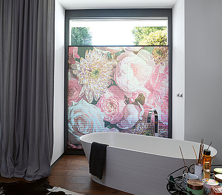 Plissee mit grossem Blumenmotiv im Badezimmer als halbtransparenter Sichtschutz vor bodentiefem Fenster