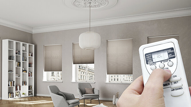 Wohnzimmer mit geschlossenen Wabenplissees an den Fenstern und Hand mit Fernbedienung zur Temperaturregelung.