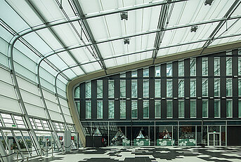 Grosses, lichtdurchflutetes Hoteldach mit gebogenen MHZ-Sonnenschutzsegeln vor einer modernen Glasfassade.