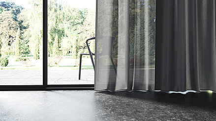 Nahaufnahme eines weissen MHZ-Stores und eines grauen Vorhangs vor einem grossen Fenster mit Blick ins Grüne.