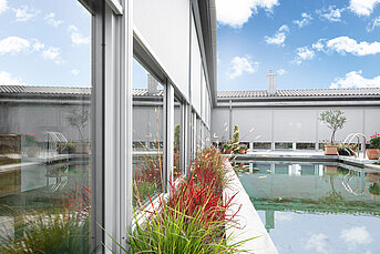 Fenstermarkisen an grossen Glasflächen eines modernen Gebäudes mit Innenhof und Poolbereich