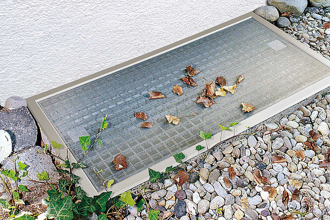Lichtschachtabdeckung Lisa auf Kiesbett mit Laub auf dem Edelstahlgewebe, schützt vor Schmutz und Kleintieren