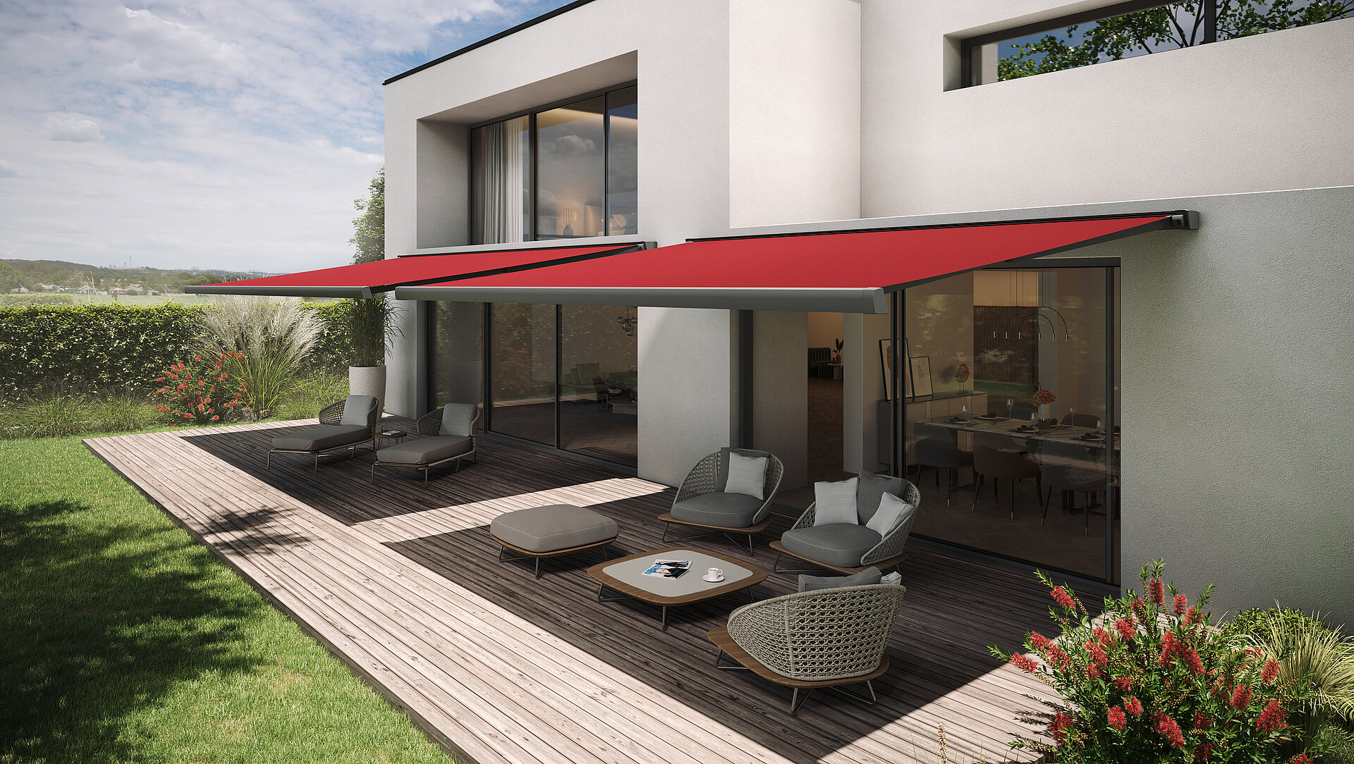 Zwei rote Gelenkarmmarkisen über Terrasse eines modernen Hauses mit Sitzgruppe auf Holzdeck.