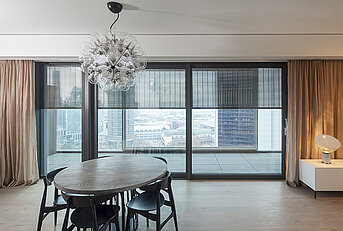Wohnbereich in einem Hochhaus mit s_enro-Metallbehang von MHZ, durch den die Skyline von Frankfurt sichtbar ist.