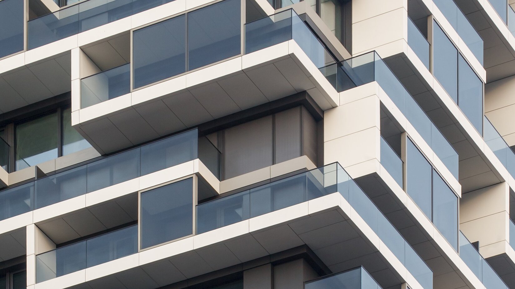 Detailansicht moderner Fassade mit Glasbalkonen und teilweise geschlossenem Sonnenschutz vor den Fensterflächen.